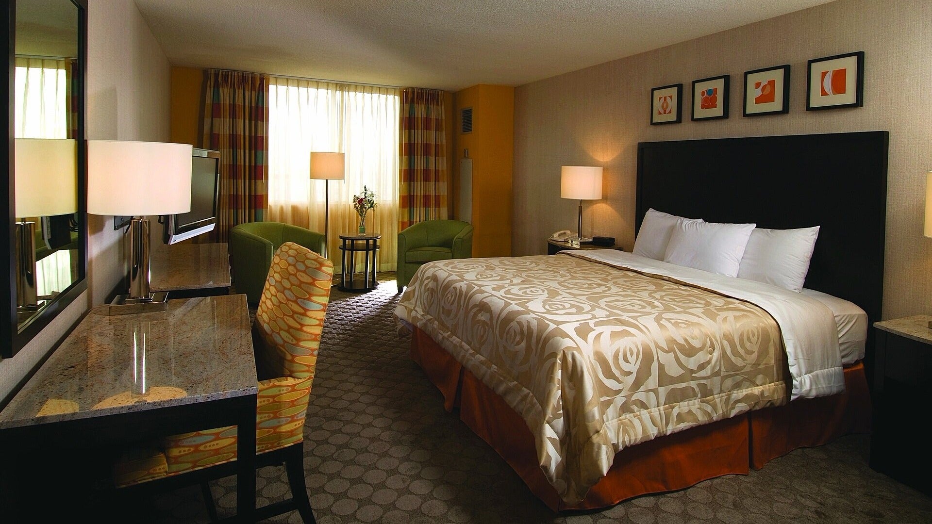 hotel room with bed, artwork, seating, work desk and curtains