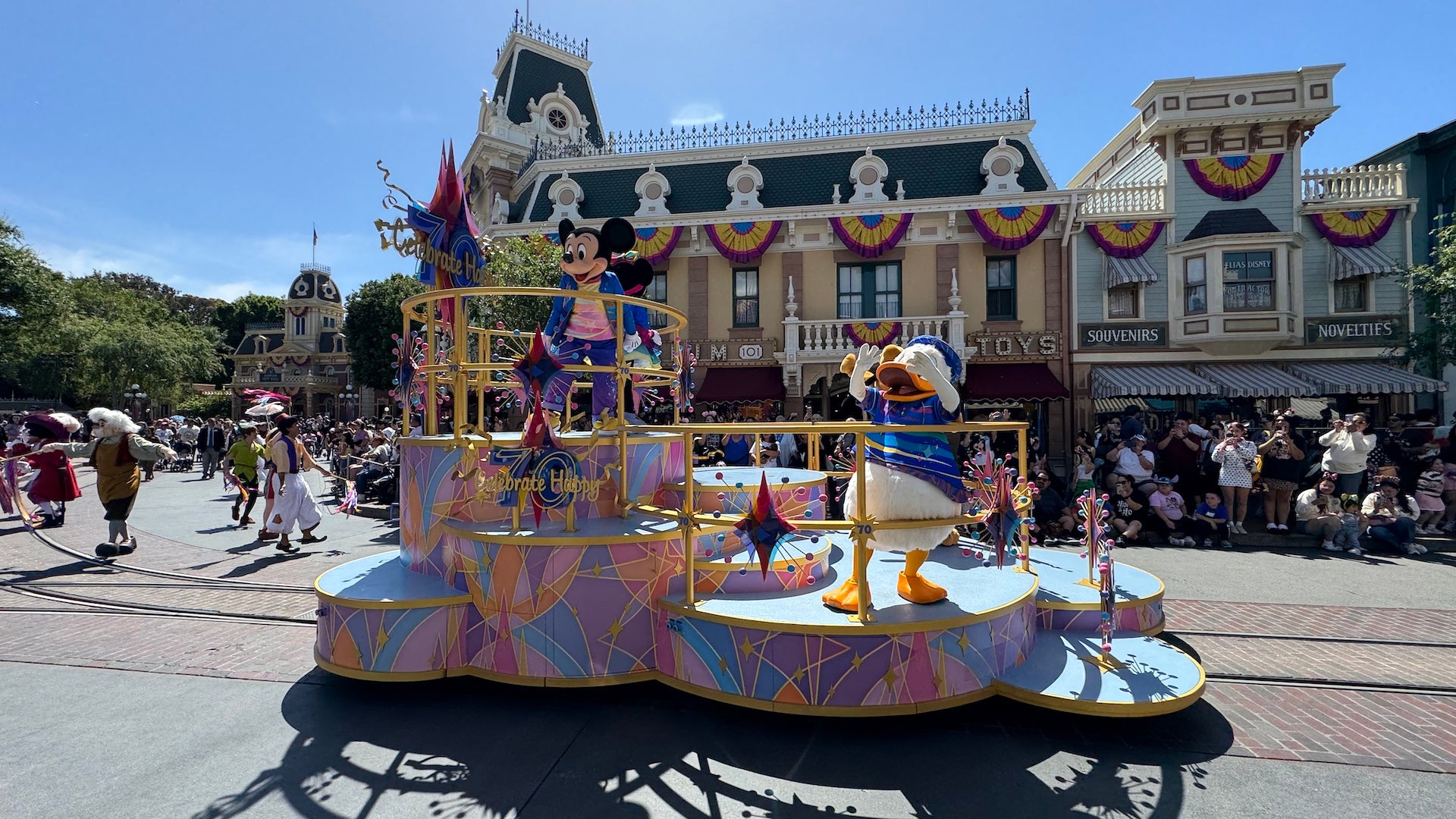 A parade float with 70th celebration decor and mickey and Donald on top waving to the crowd as they go down Main Street USA at Disneyland