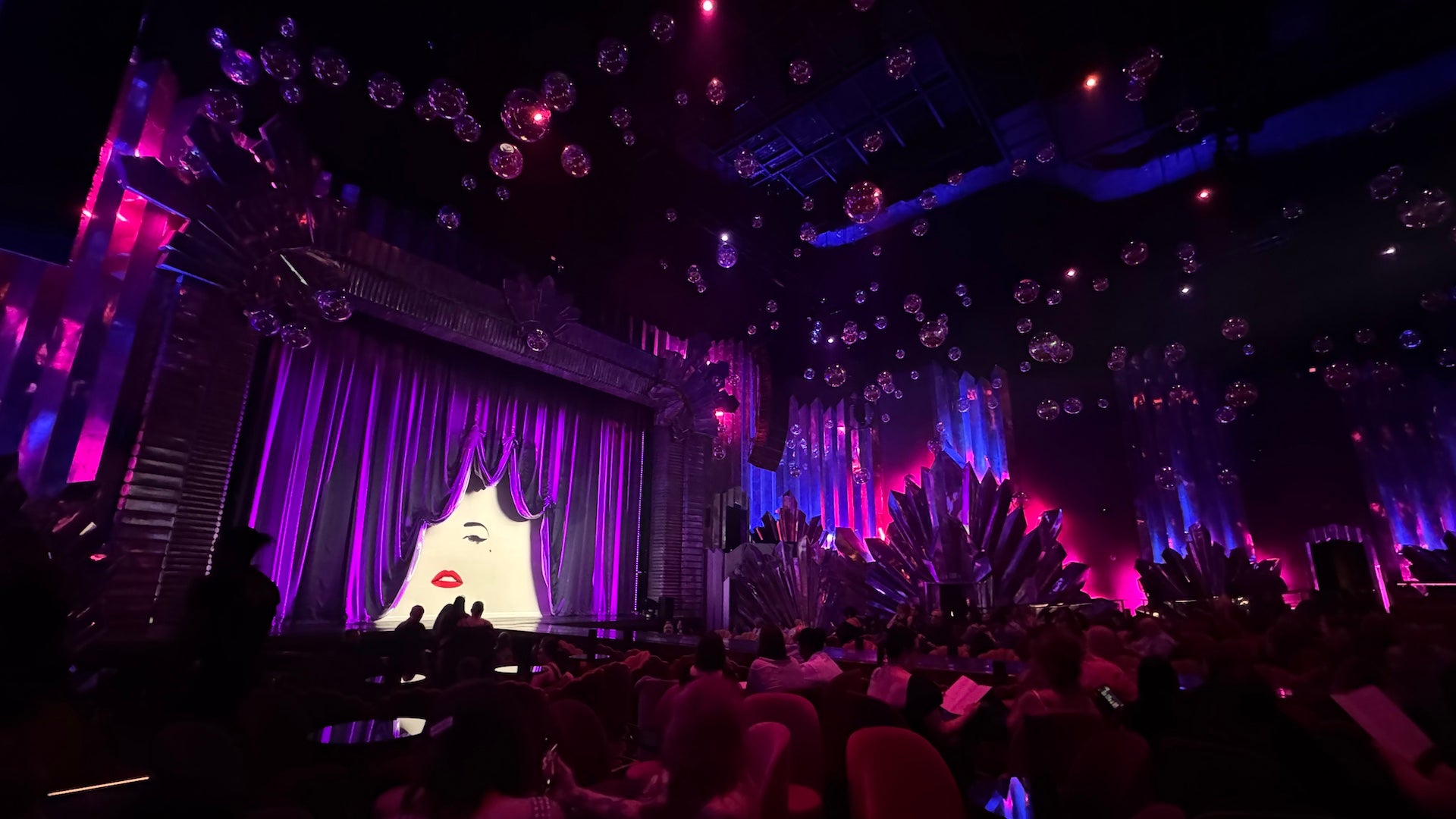 Inside a theater in Las Vegas with red velvet seating, pink and blue lighting and maximalist vintage vibes