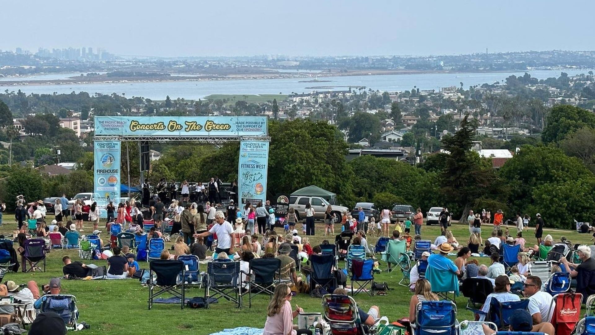 people in a park sitting and talking while watching a concert, overlooking san diego