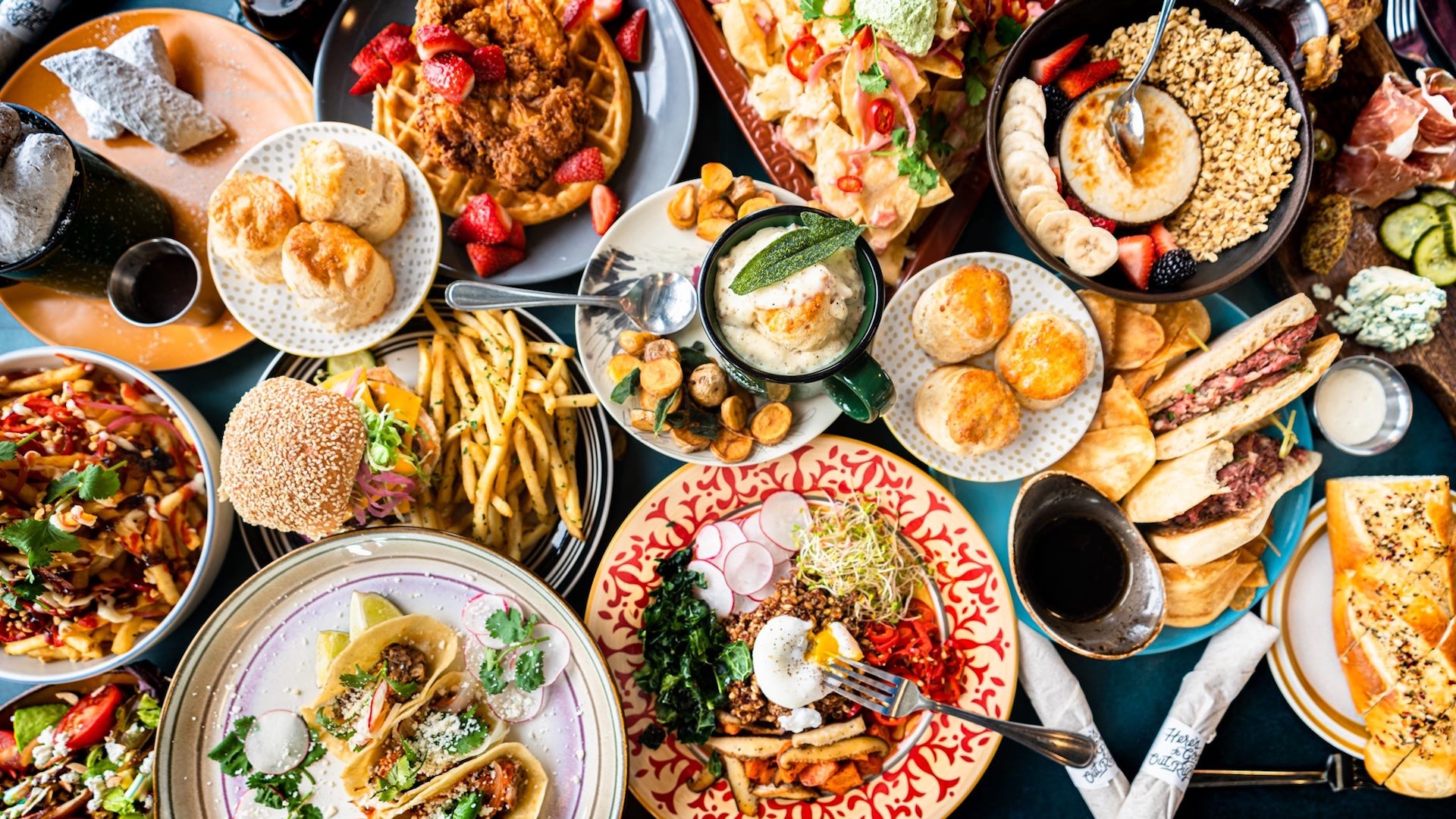 a lot of plates with food like burgers, fries, waffles, tacos