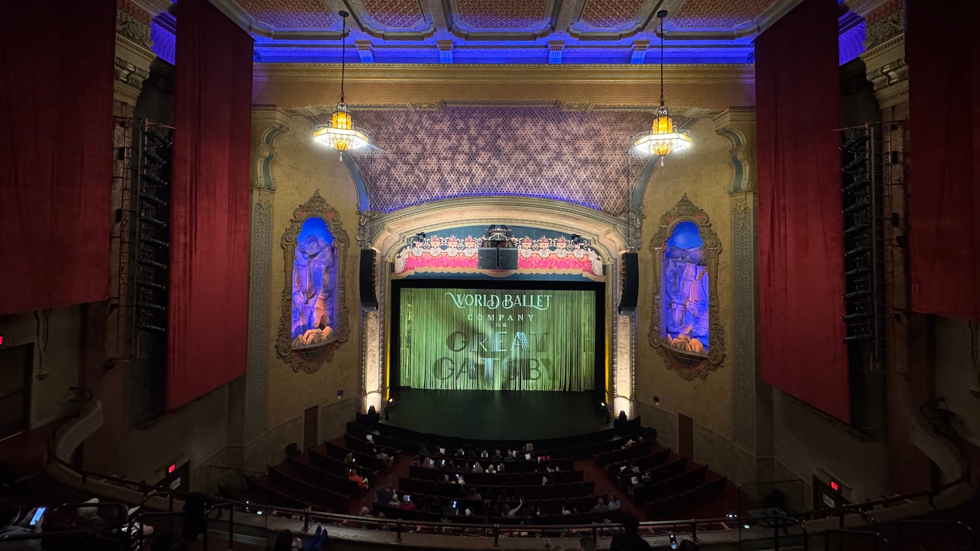 Interior of a theater with a stage and red drapes hanging from the walls
