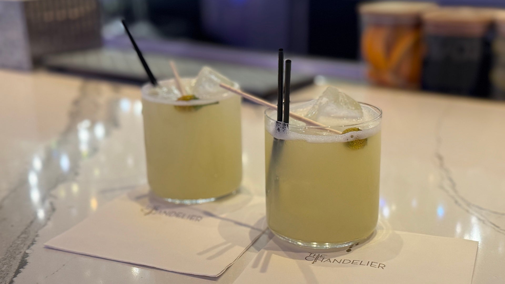 Two margaritas on a marble bar top with flower buds in each