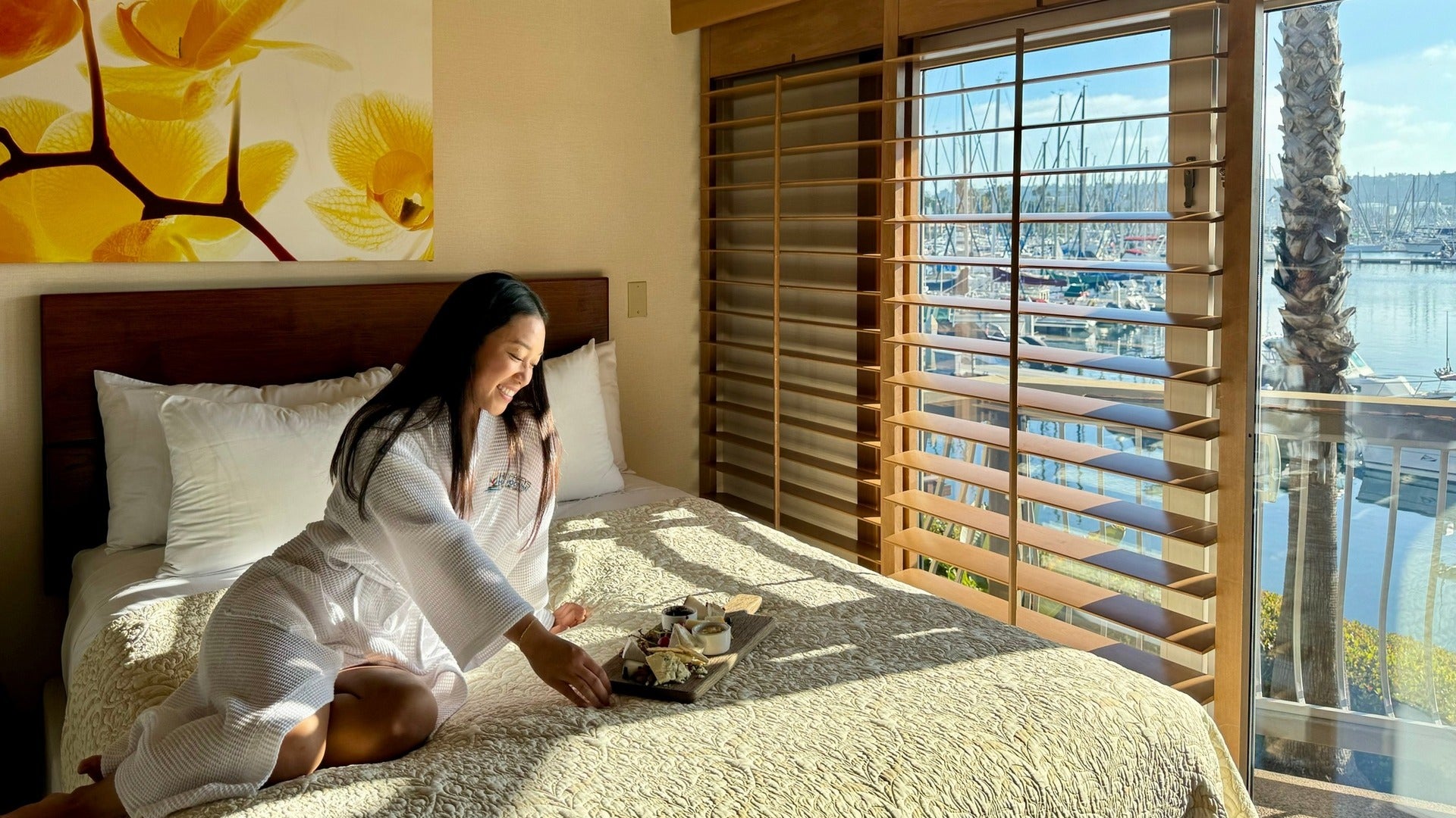 woman in bed with a plate of food and view of marina