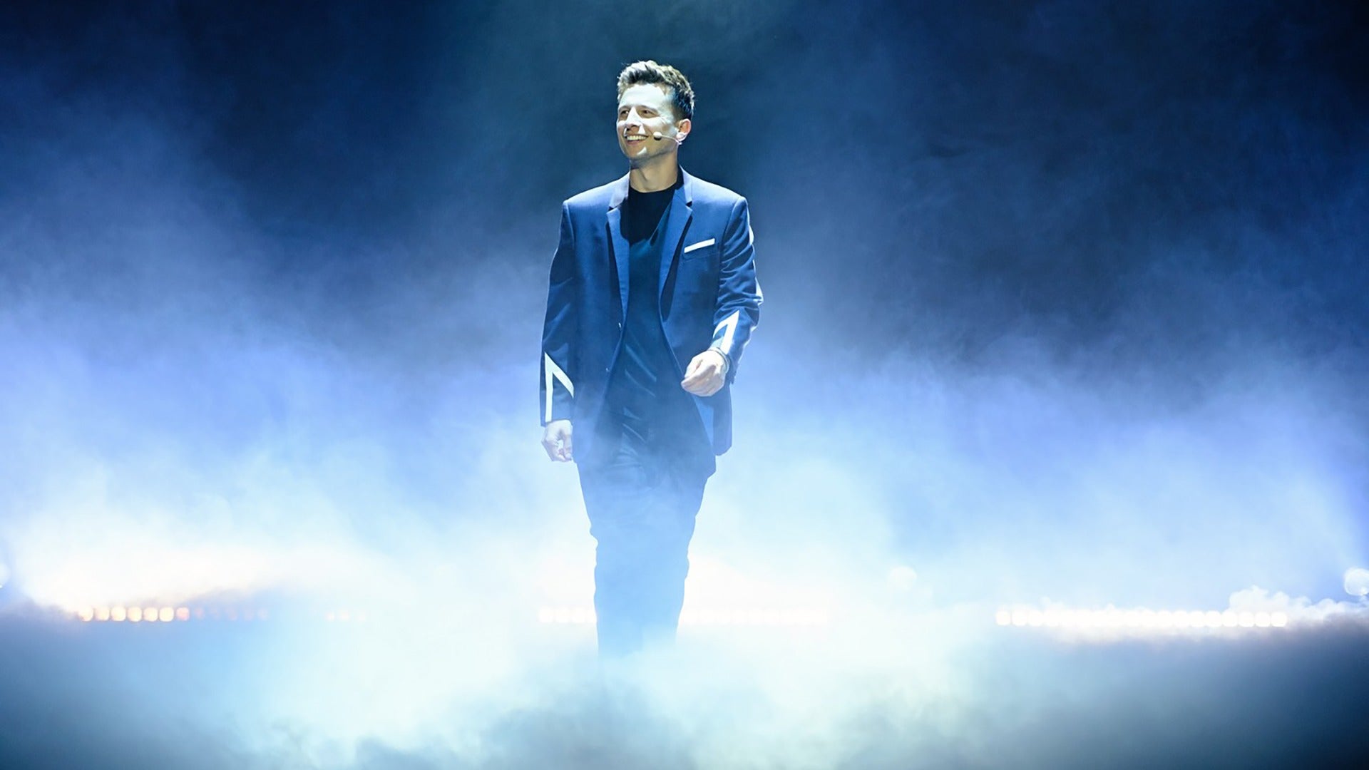 man on stage wearing a tux and microphone