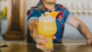 man handing over a cocktail drink with orange garnish