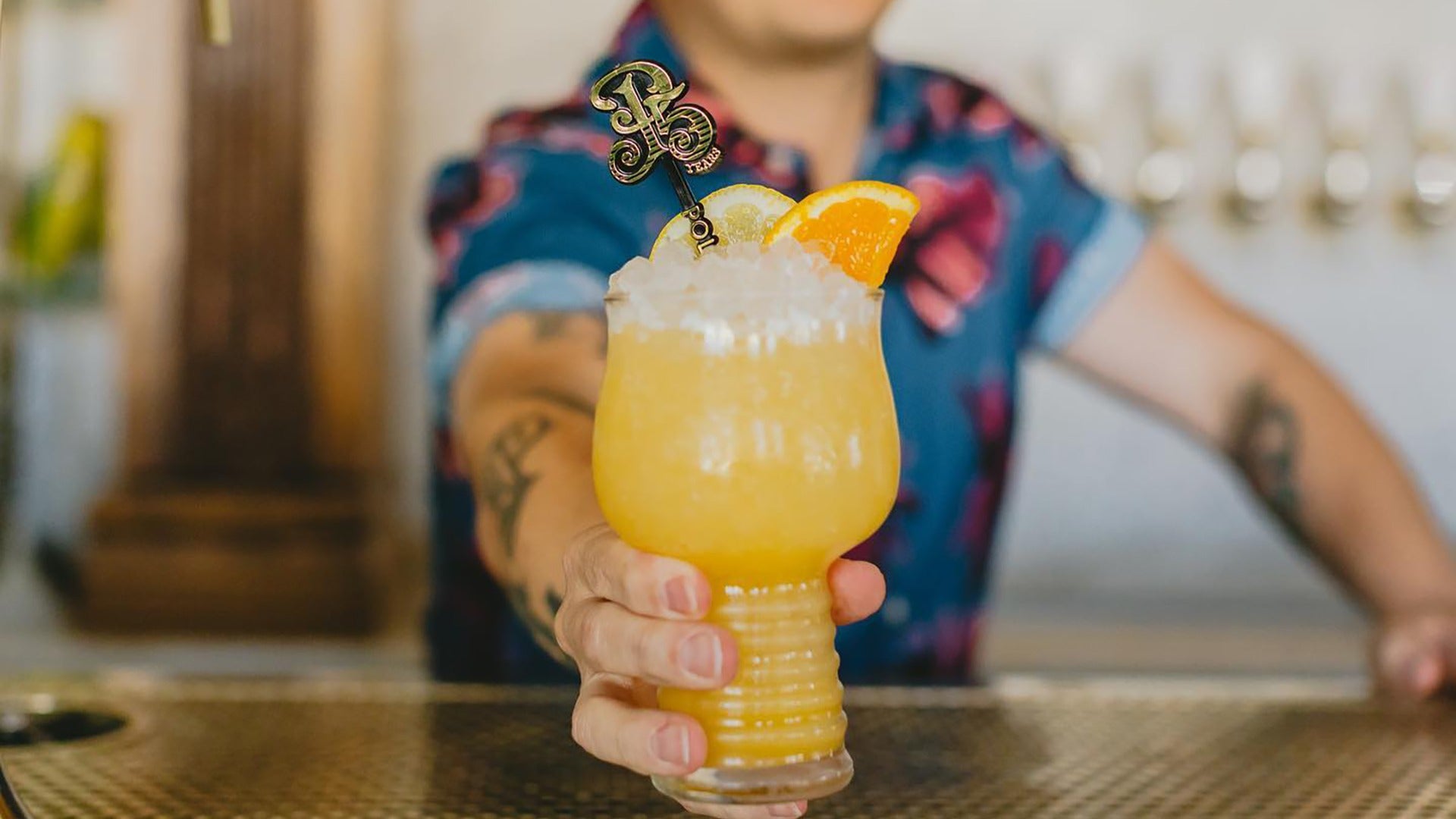 man handing over a cocktail drink with orange garnish