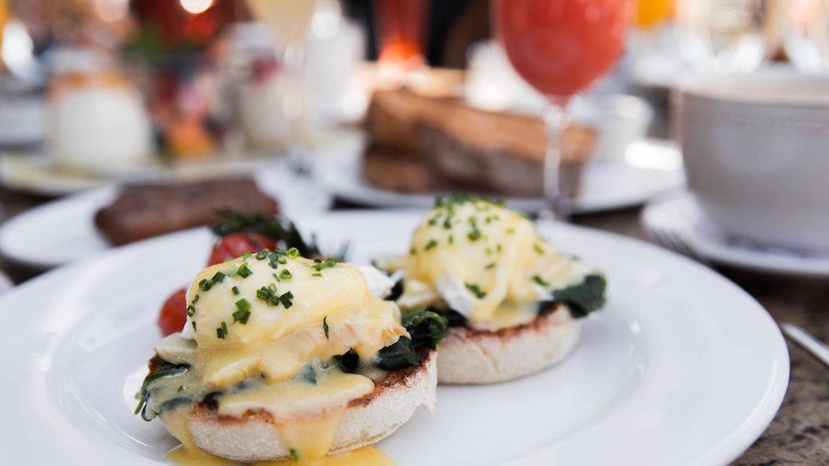 Close-up of eggs Benedict served on toasted English muffins with sautéed spinach, poached eggs, and hollandaise sauce, garnished with chives and served with roasted tomatoes at Mon Ami Gabi in Las Vegas.