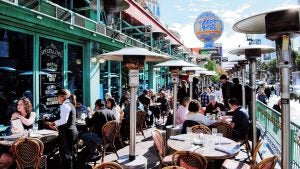 Bustling outdoor patio of Mon Ami Gabi on the Las Vegas Strip, filled with diners enjoying meals under heat lamps and shaded tables, with the Eiffel Tower replica and Paris Las Vegas balloon sign visible in the background.