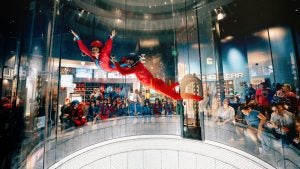kid being guided by an indoor skydiving instructor with people watching