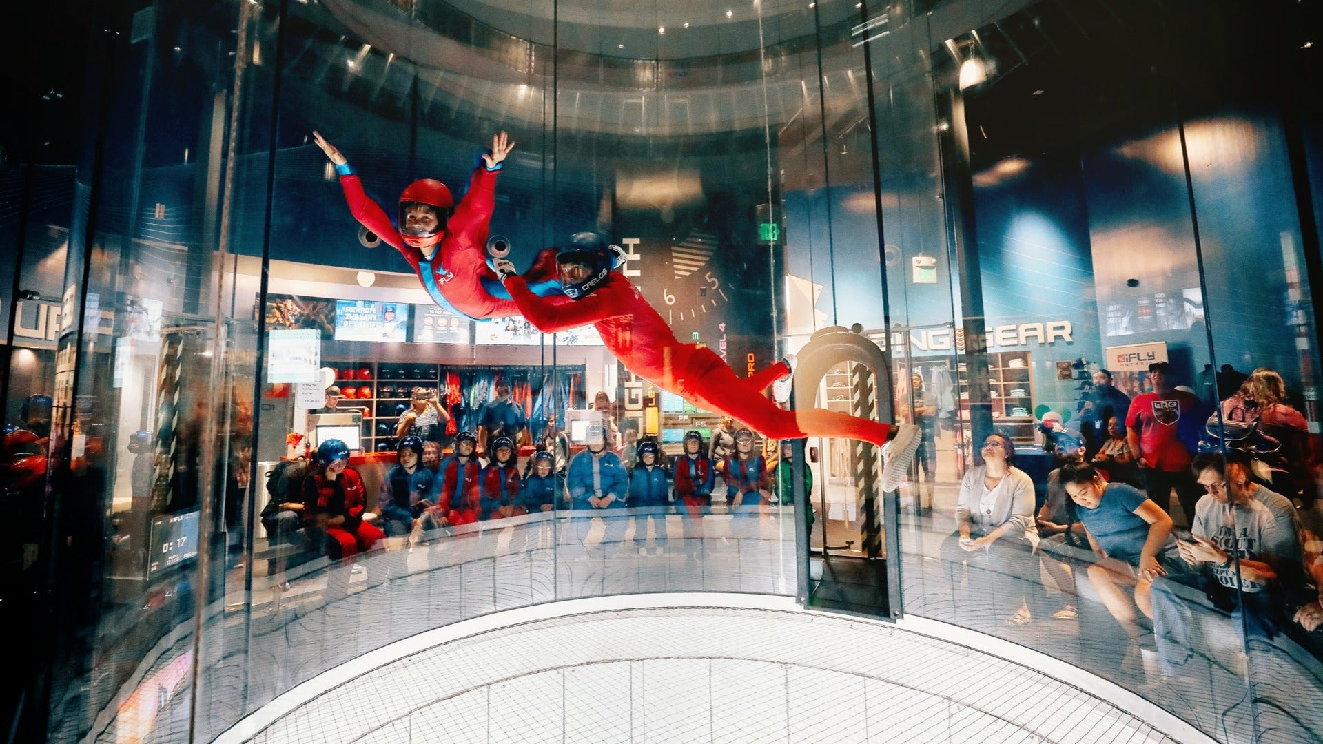 kid being guided by an indoor skydiving instructor with people watching