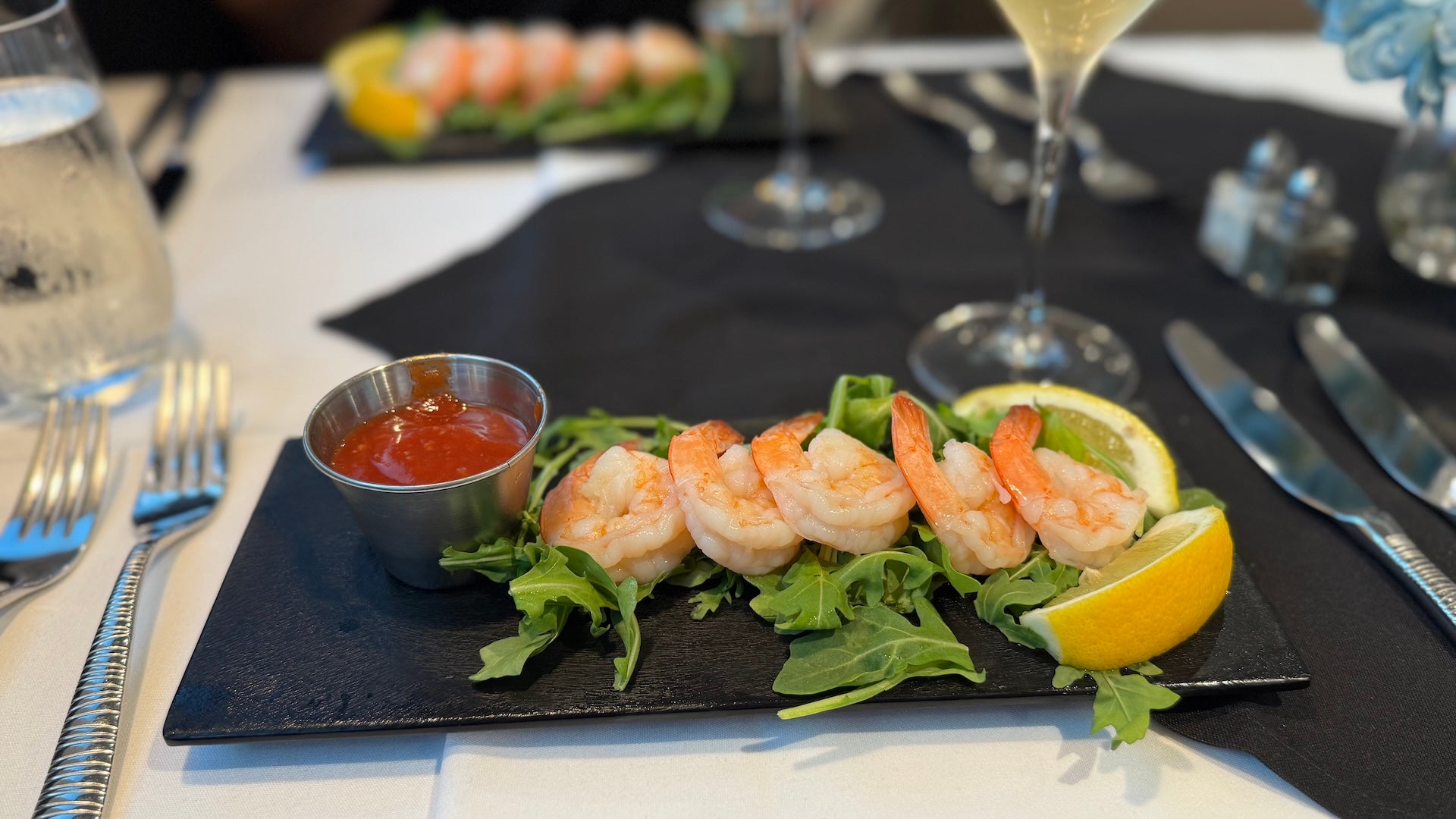 Shrimp cocktail on a plate with lemons and cocktail sauce on a dinner table with champagne
