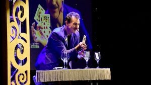magician holding cards with wine glasses on stage