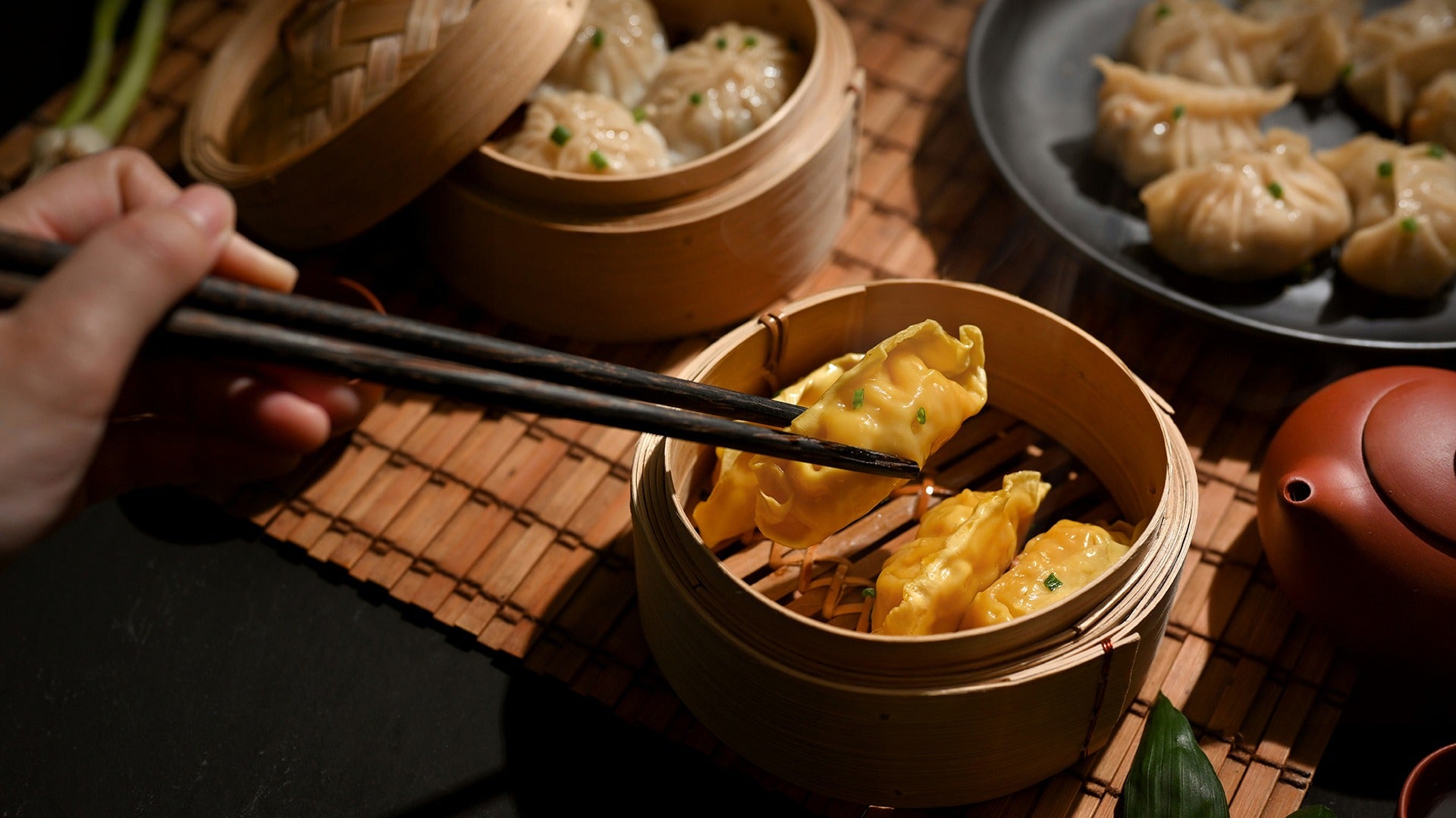 person holding chopsticks grabbing dim sum with other dumplings on the side