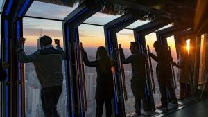 people leaning on a glass observation deck with a view of the city