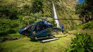 helicopter parked in a forest with a waterfall at the back