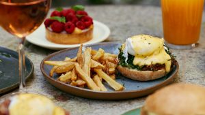eggs benedict with a side of fries, champagne, and pastry at the back