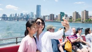 mom and daughter taking a selfie on a cruise with nyc skyline behind