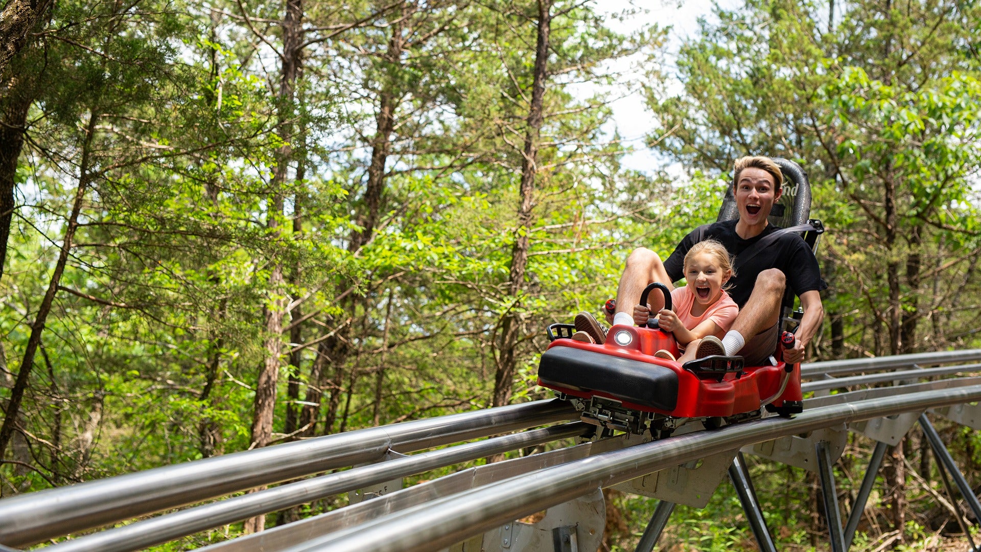man and child on a mountain coaster passing through a forest