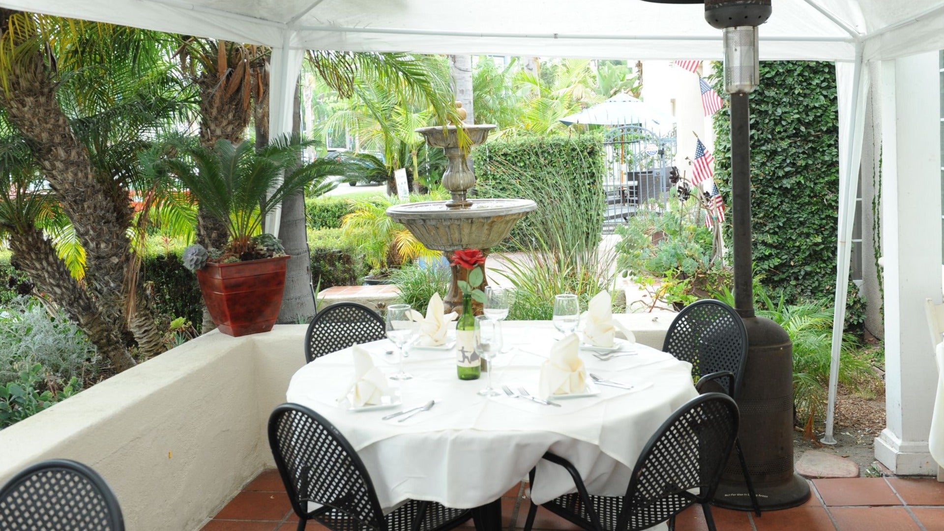 outdoor restaurant patio with table setting, heater, and fountain at the back