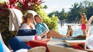 family relaxing on pool chairs with children and dolphins at the back