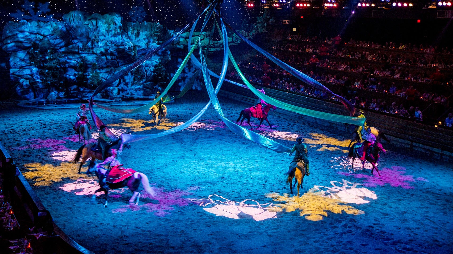 group pf performers on horseback holding fabrics draped from the ceiling with an audience