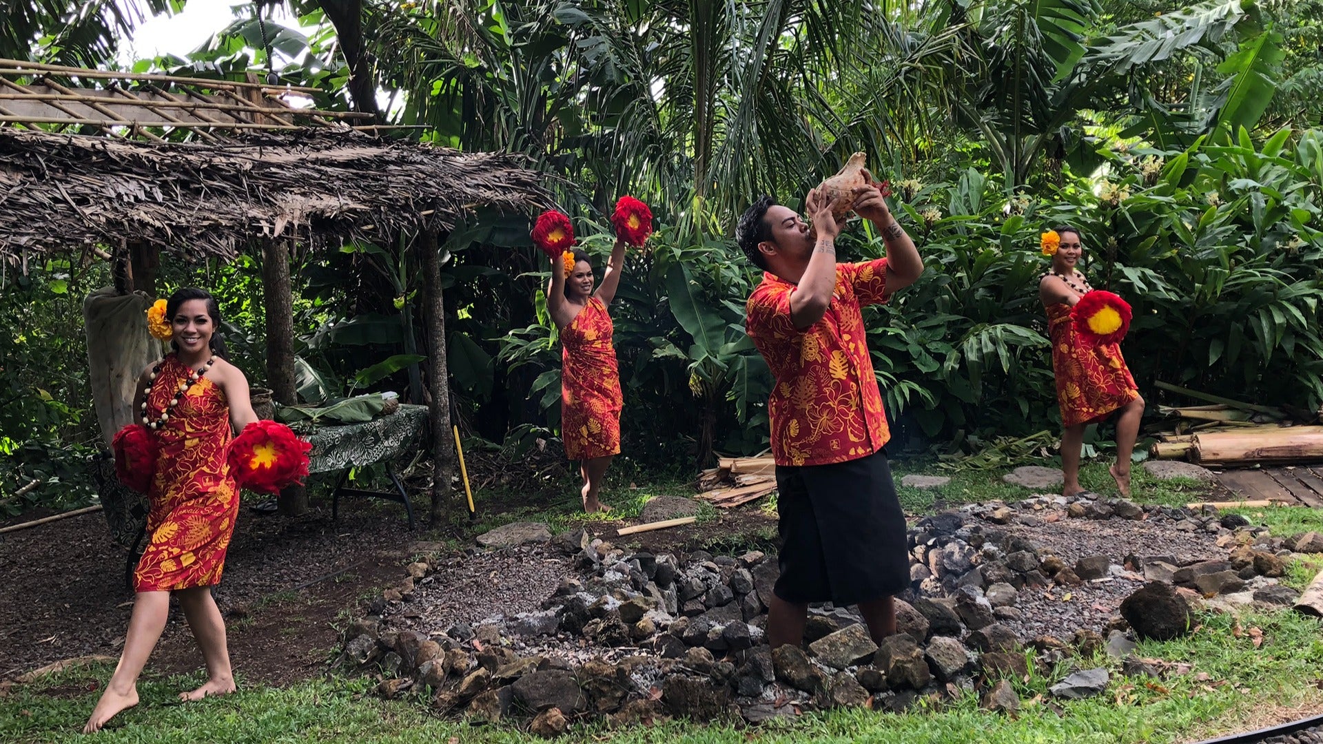 a luau with a man blowing on a conch and women in leis
