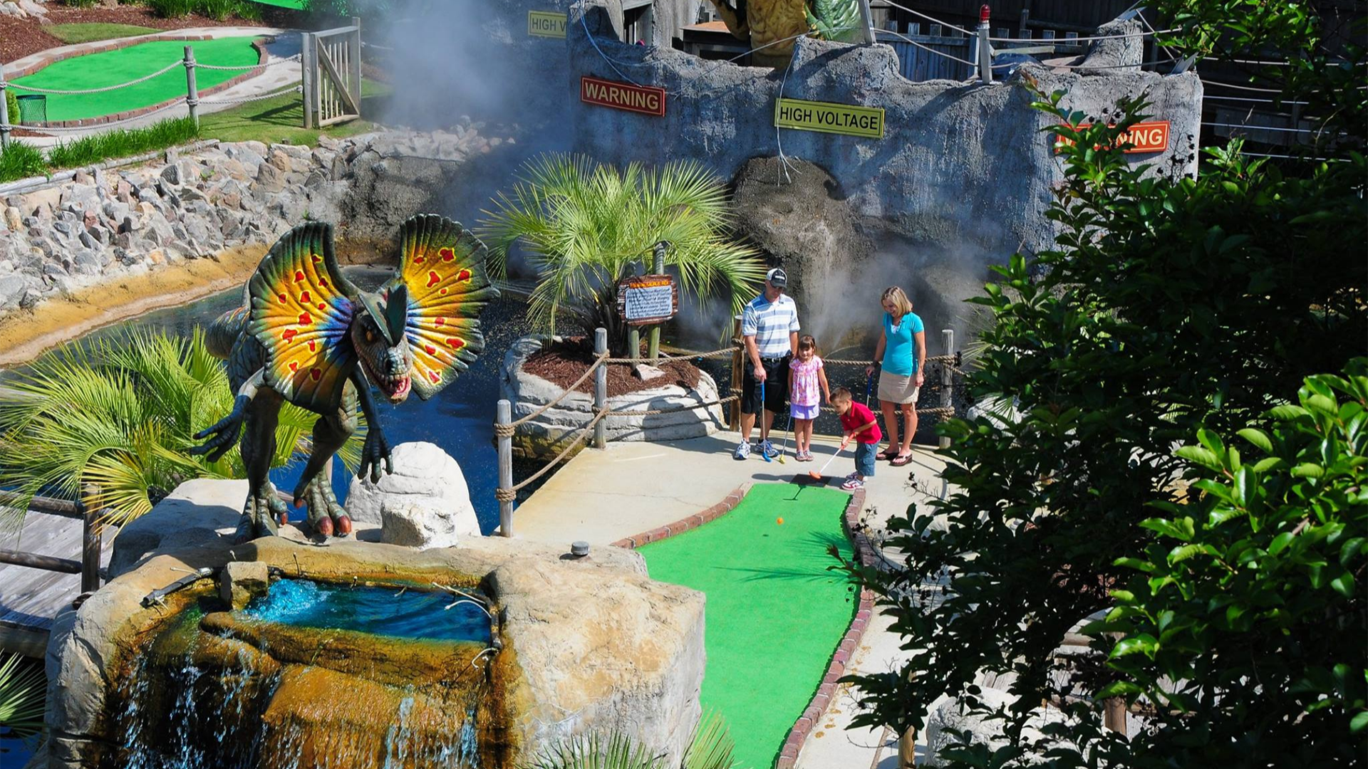 a family with kids playing mini golf, dinosaur statue in the middle