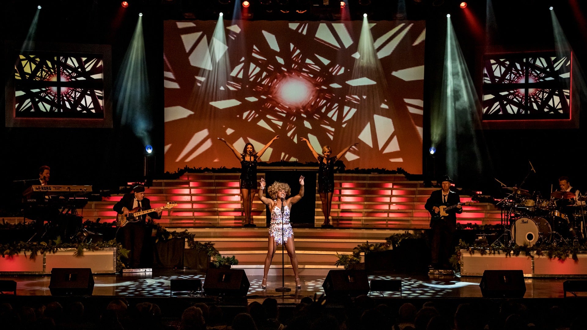a performer in costume on stage with a band and backup singers