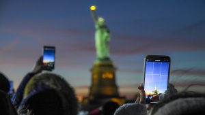 people taking a photo of the statue of liberty at night