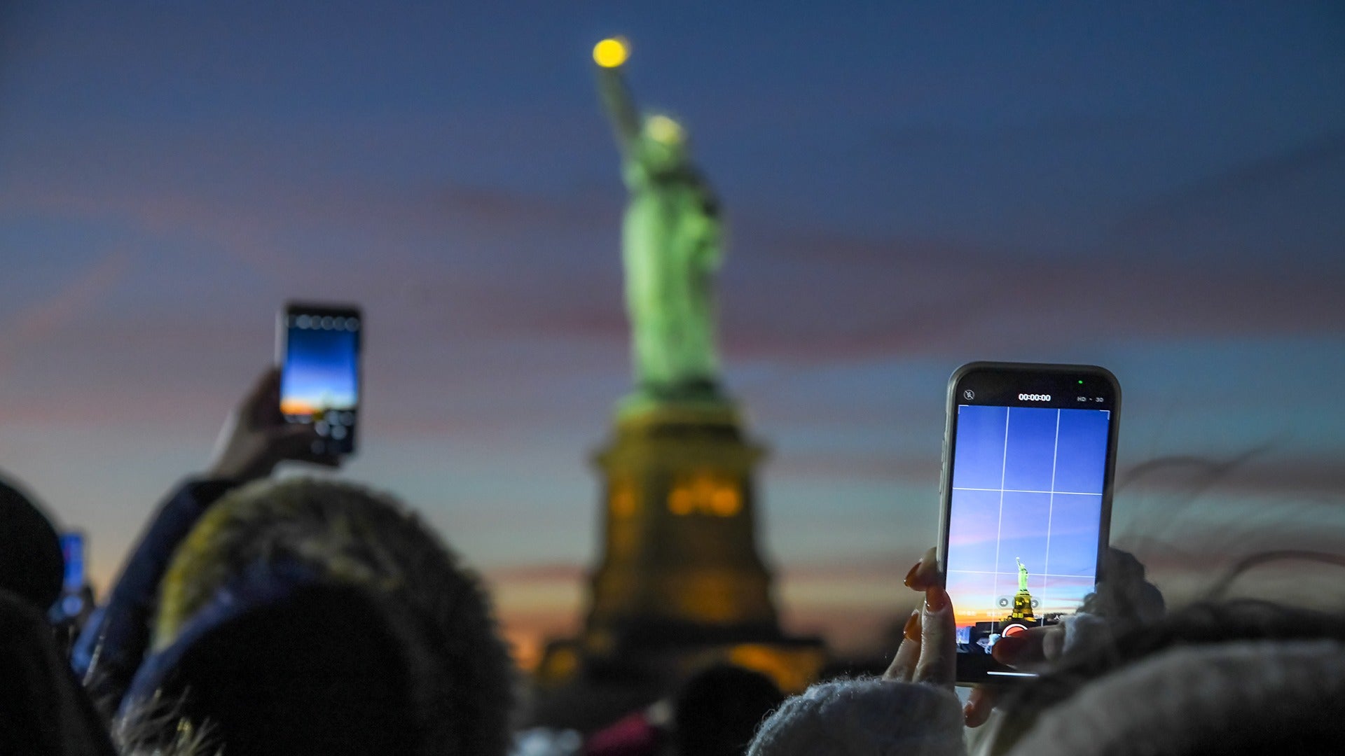 people taking a photo of the statue of liberty at night