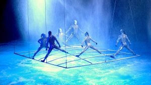 acrobats in costume standing on a metal bar above water