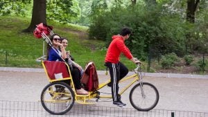 people riding a pedicab through the park with a driver