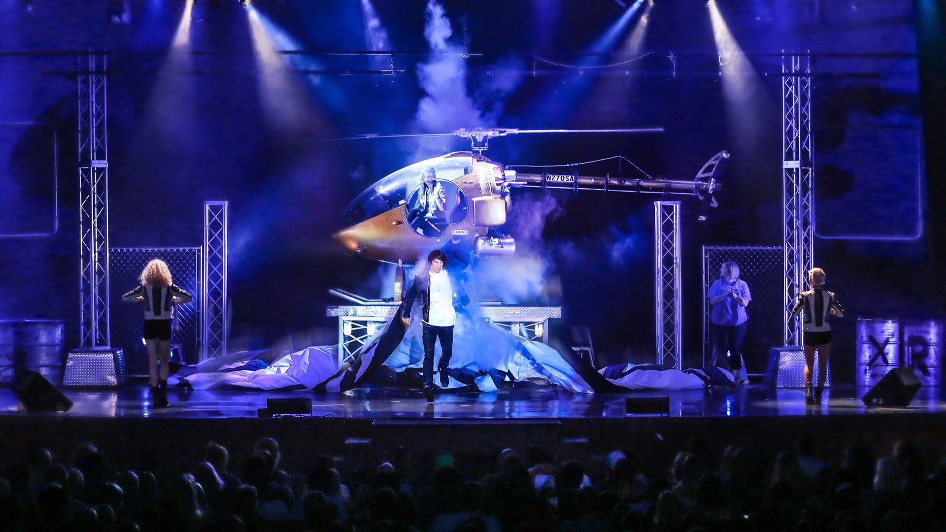 man performing on stage with visuals of a helicopter