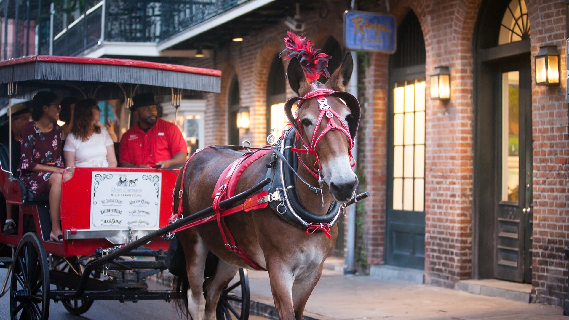 horse drawn carriage with passengers passing by a brick building