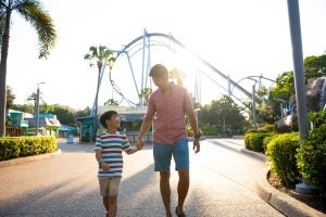 father and son walking hand in hand with a roller coaster at the back