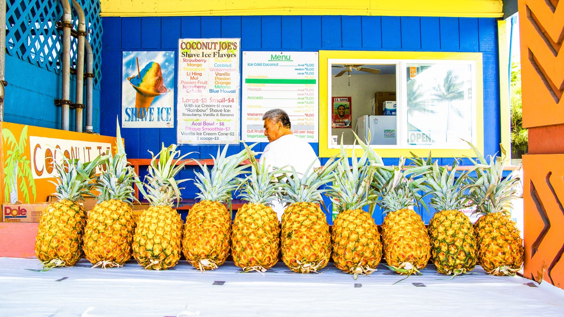 man selling pineapples with a store window behind him