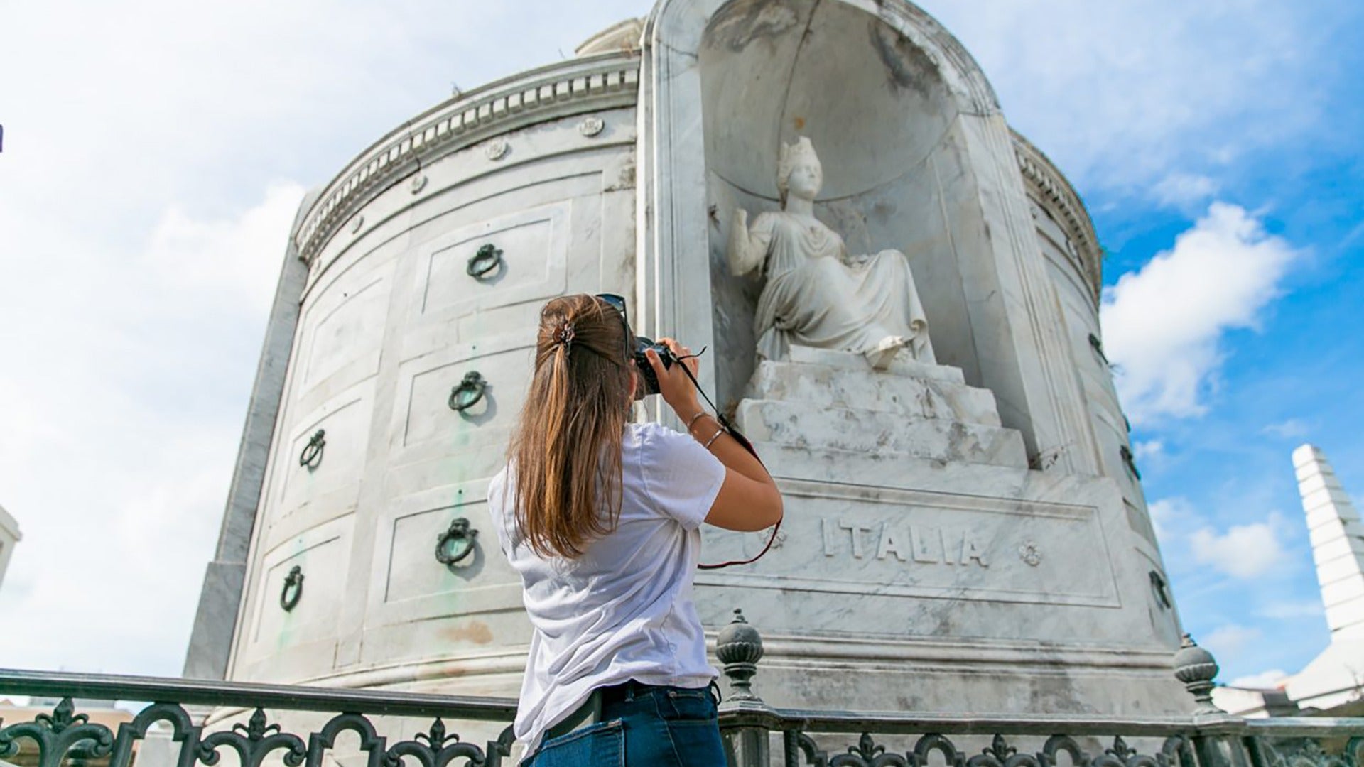 a girl taking a photo of a cemetery statue