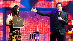 a mentalist on stage with a volunteer holding a chalk board