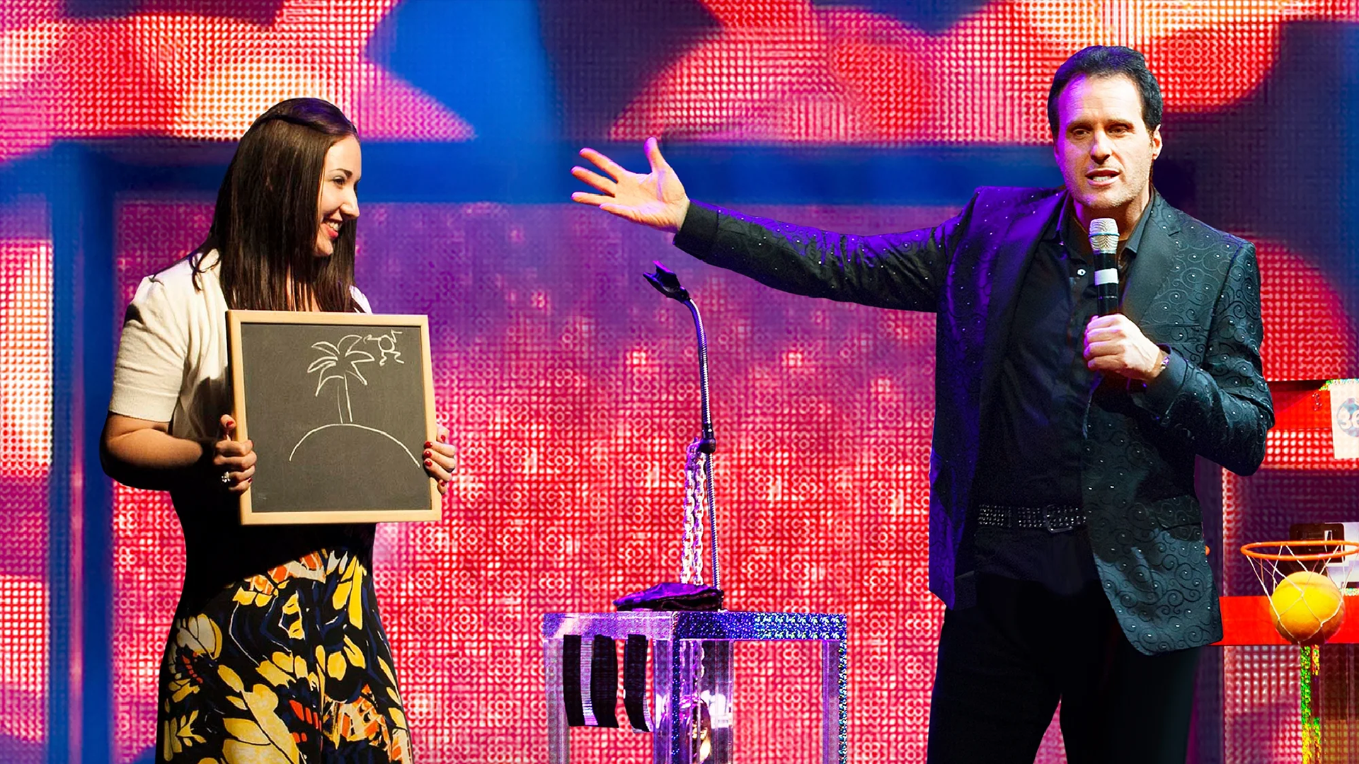 a mentalist on stage with a volunteer holding a chalk board