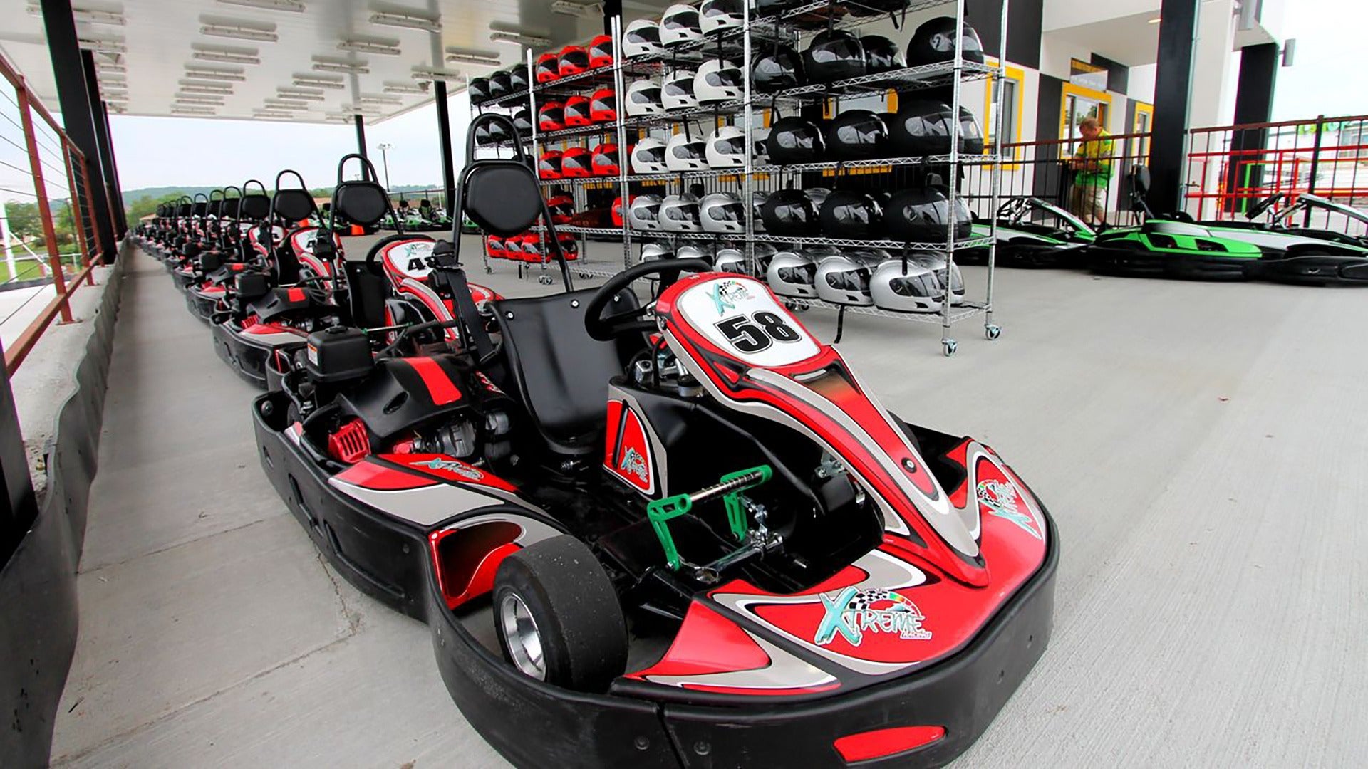 go karts in line at a track with a shelf of helmets on the side