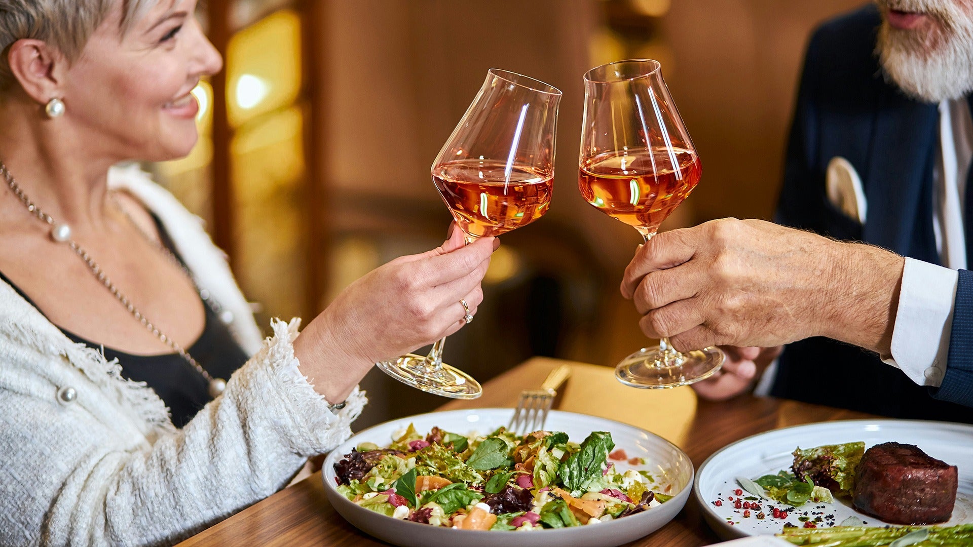 couple toasting wine, salad and steak on the table