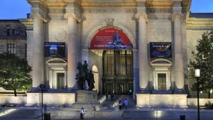a museum exterior with a statue of theodore roosevelt in front and people walking
