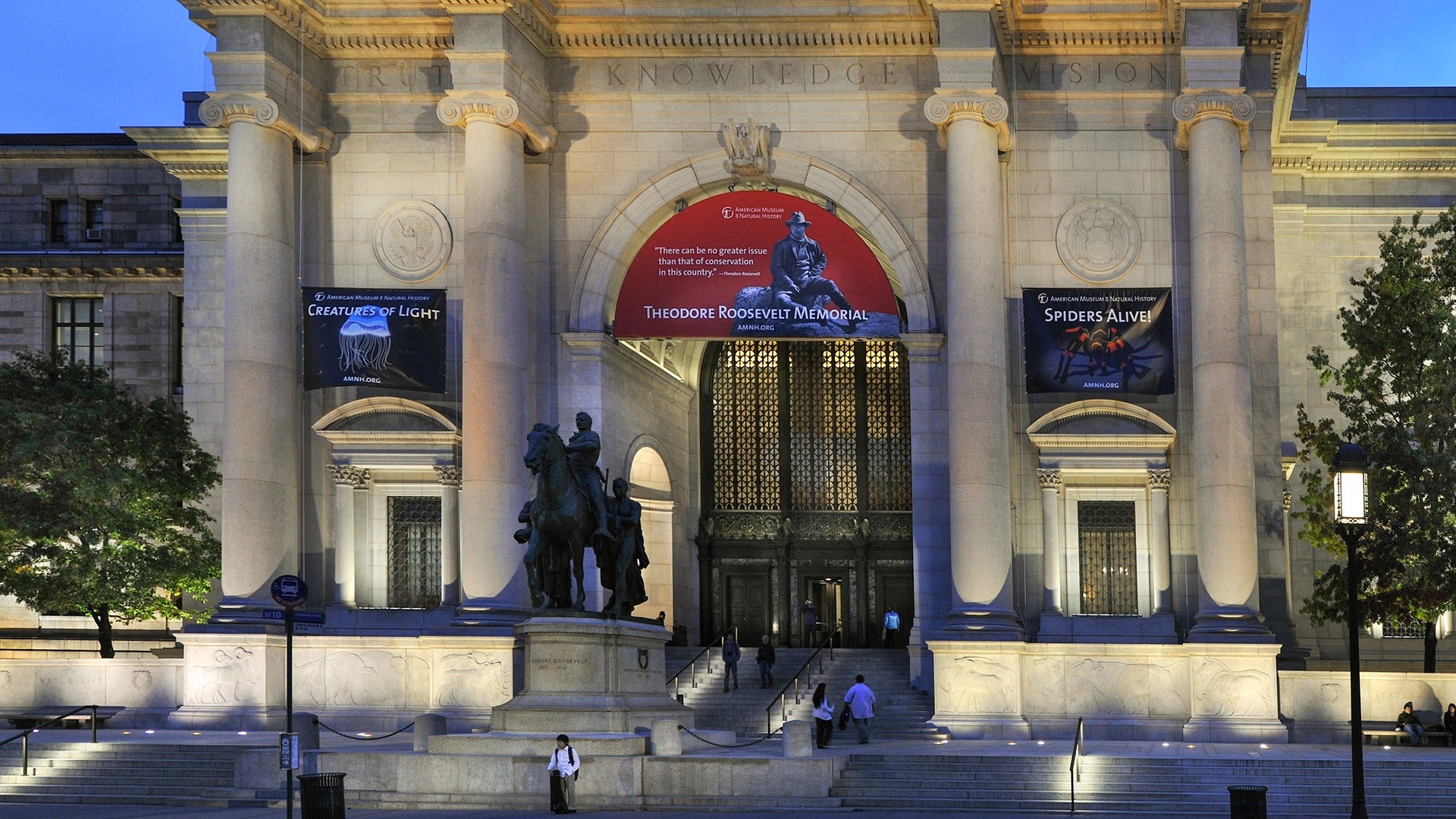 a museum exterior with a statue of theodore roosevelt in front and people walking