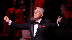 a man in suit and tie on stage holding a mic