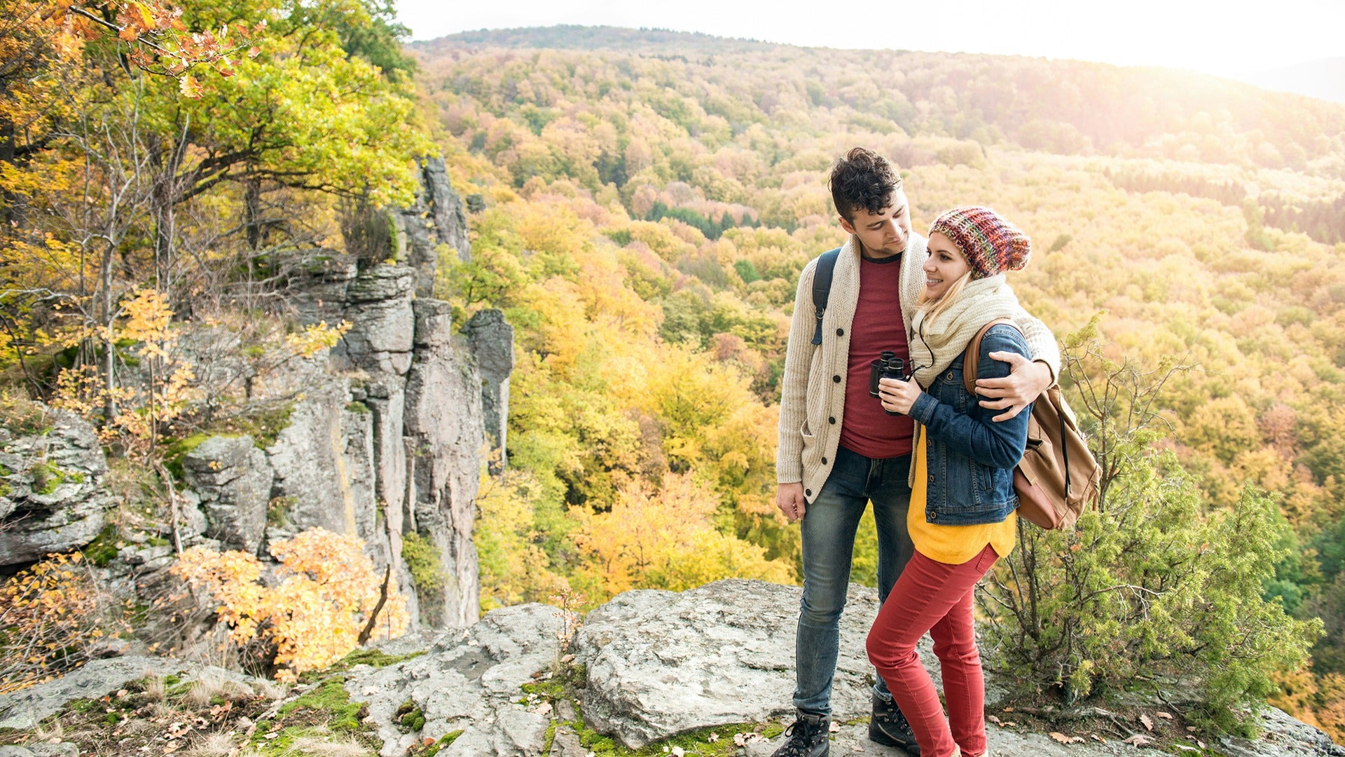 a couple hiking, girl holding binoculars on top of a mountain during fall