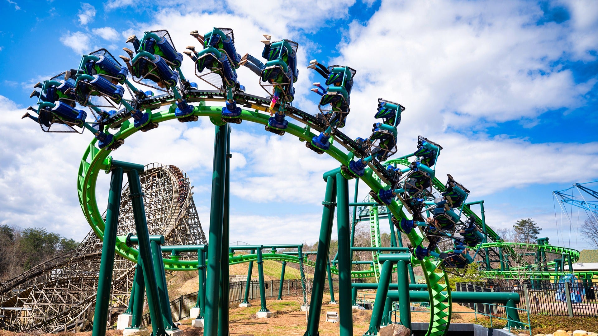 Train of Dragonflier coaster swooping around a curve, riders laughing and raising their arms