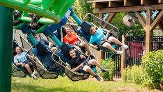 Suspended roller coaster gliding low through trees at Dollywood, with riders’ legs dangling mid-air