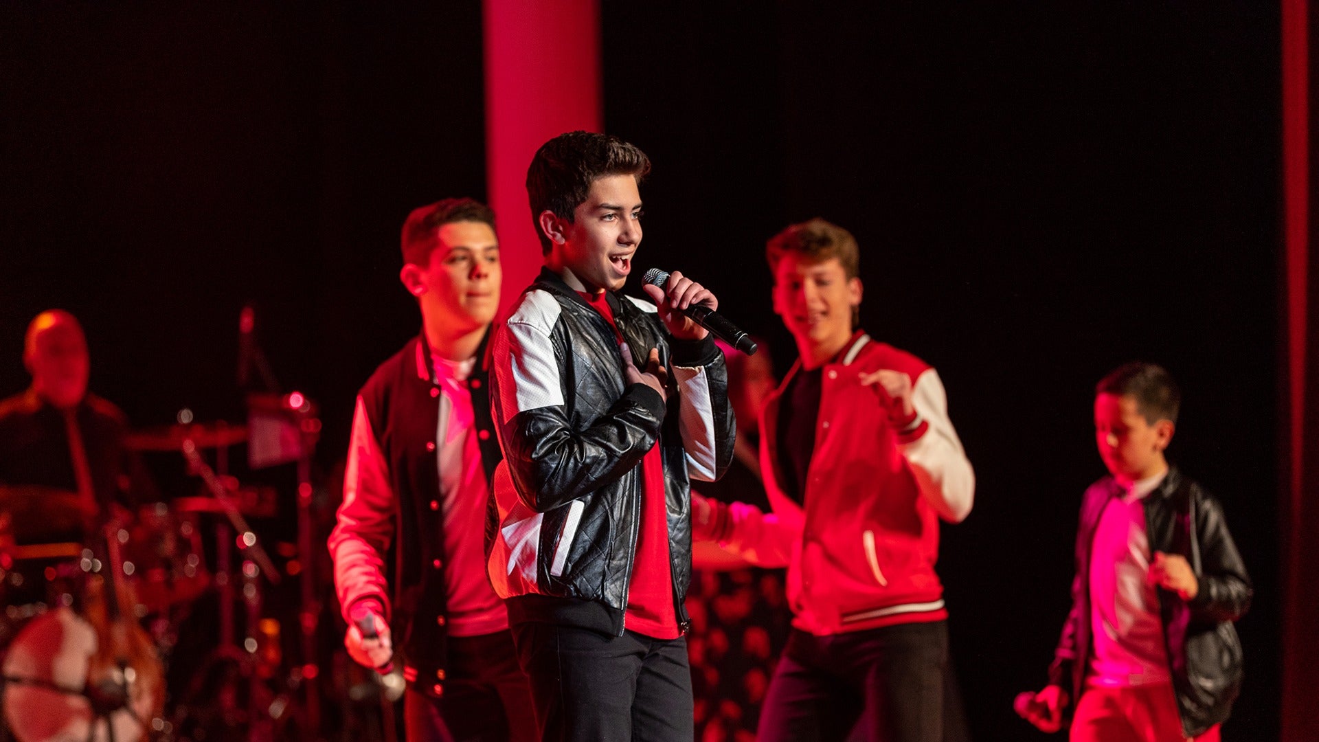 a man on stage singing with other performers behind him