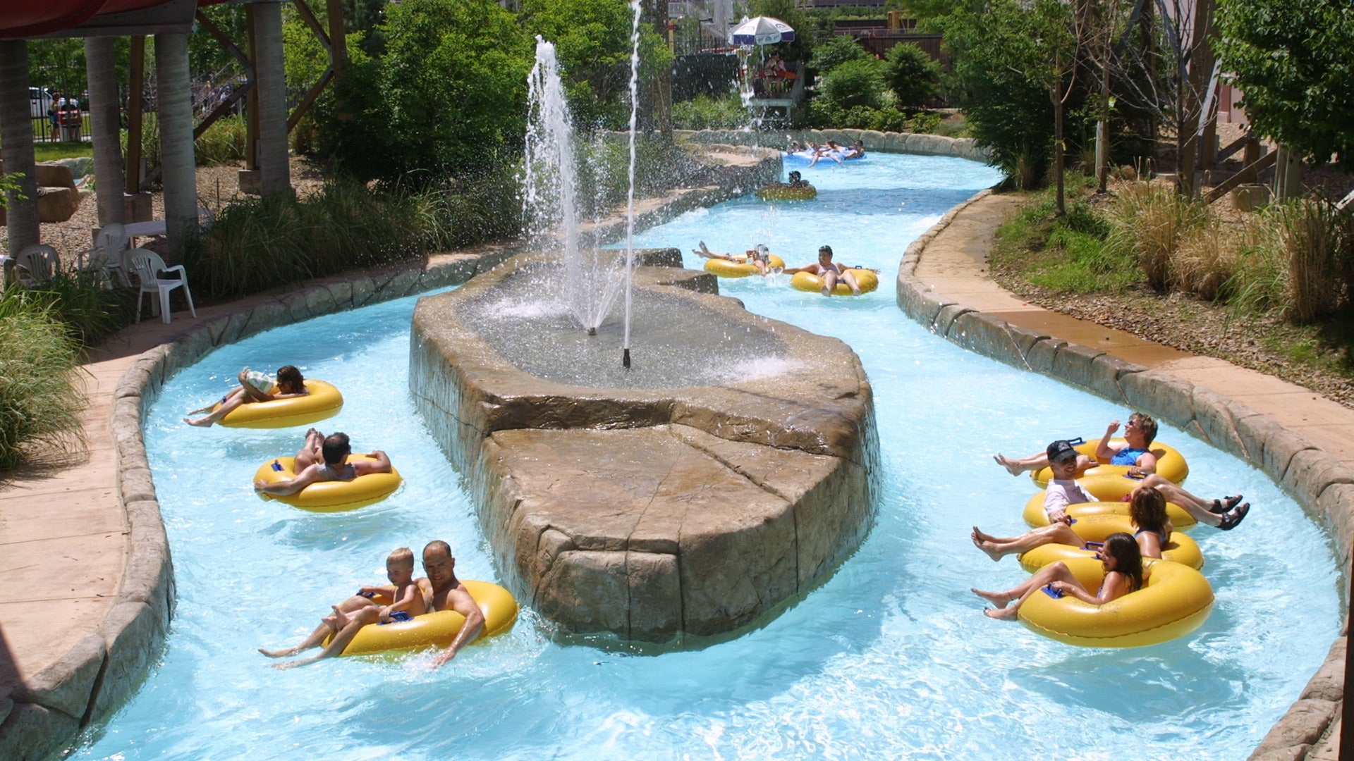 people on floaties floating down a lazy river with a fountain in the middle